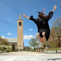 Student in cap and gown jumping with McGraw Clock Tower in the background