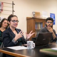 students seated around a table listening to their professor speak