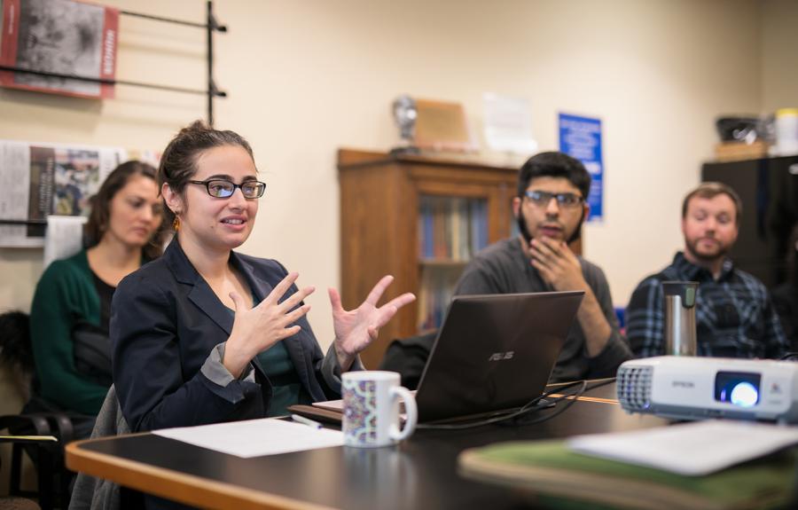 students seated around a table listening to their professor speak