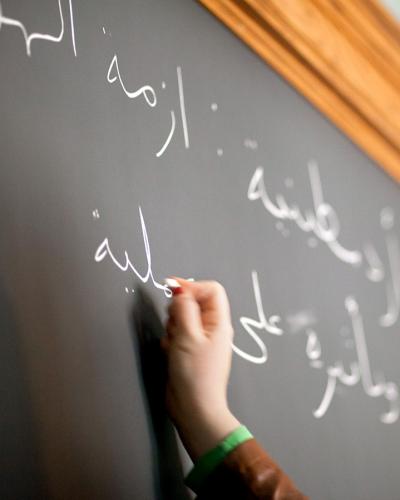 Student writes in Arabic on a chalkboard