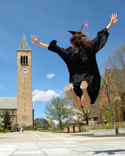 Student in cap and gown jumping with McGraw Clock Tower in the background