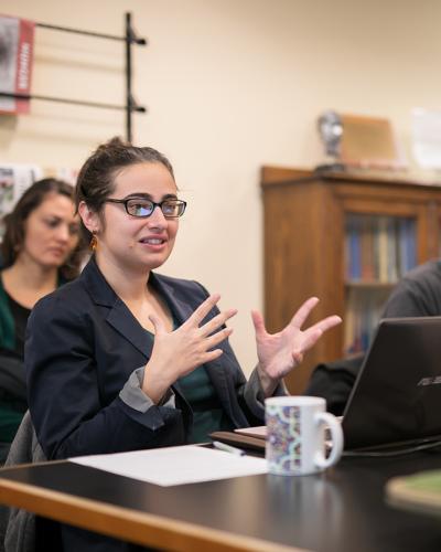 students seated around a table listening to their professor speak