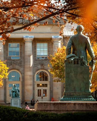 Ezra Cornell statue facing A.D. White statue and Goldwin Smith Hall, fall color on the trees