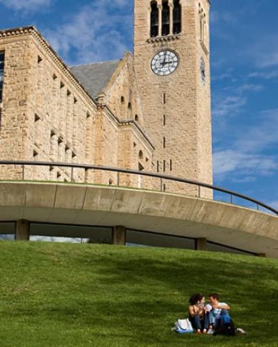 students sit on Lib Slope with Clock Tower in the background
