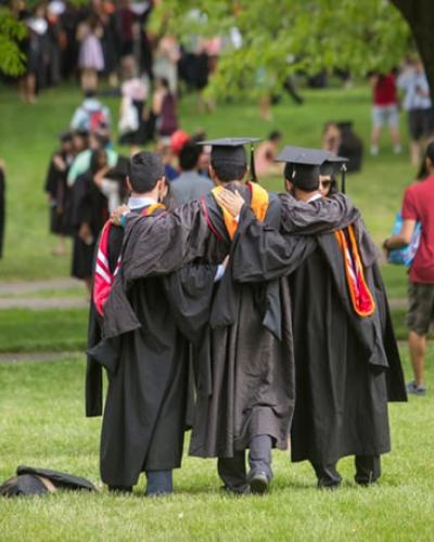 Students in cap and gown taking a photograph on the Cornell Arts Quad